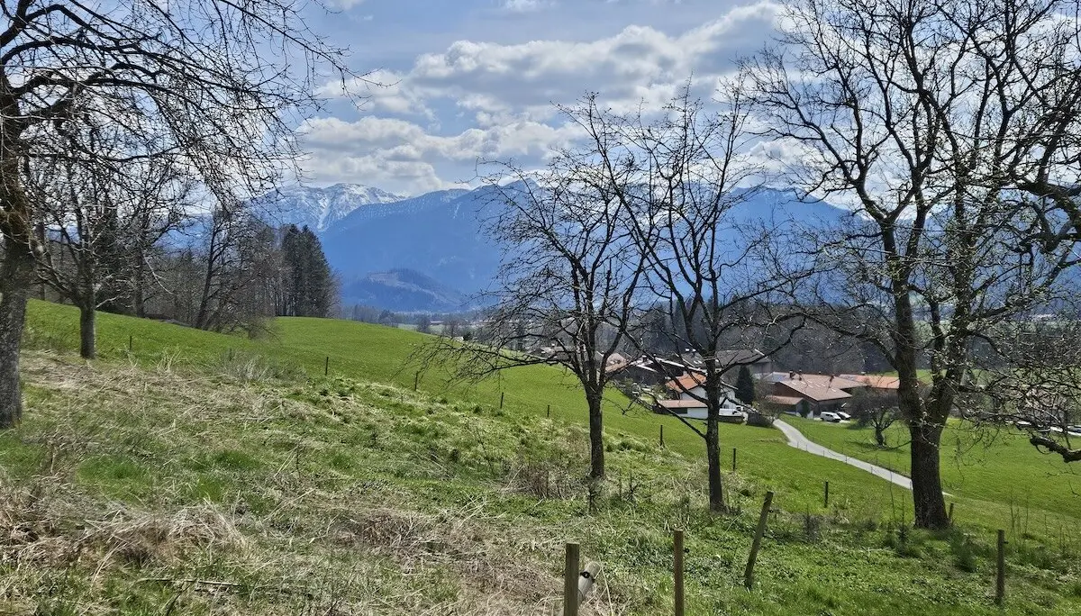 Dorf mit roten Dächern und gewundenem Weg, eingebettet in grüne Felder und Bäume, mit schneebedeckten Bergen im Hintergrund. | © DAV Markt Schwaben | Foto Hubert Inhofer