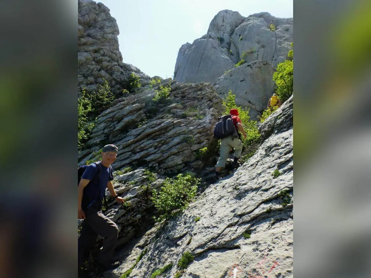Drei Wandernde mit Rucksäcken steigen einen steinigen Bergpfad hinauf; steile Felswände im Hintergrund. | © DAV Markt Schwaben | Foto Hildegard Petschik