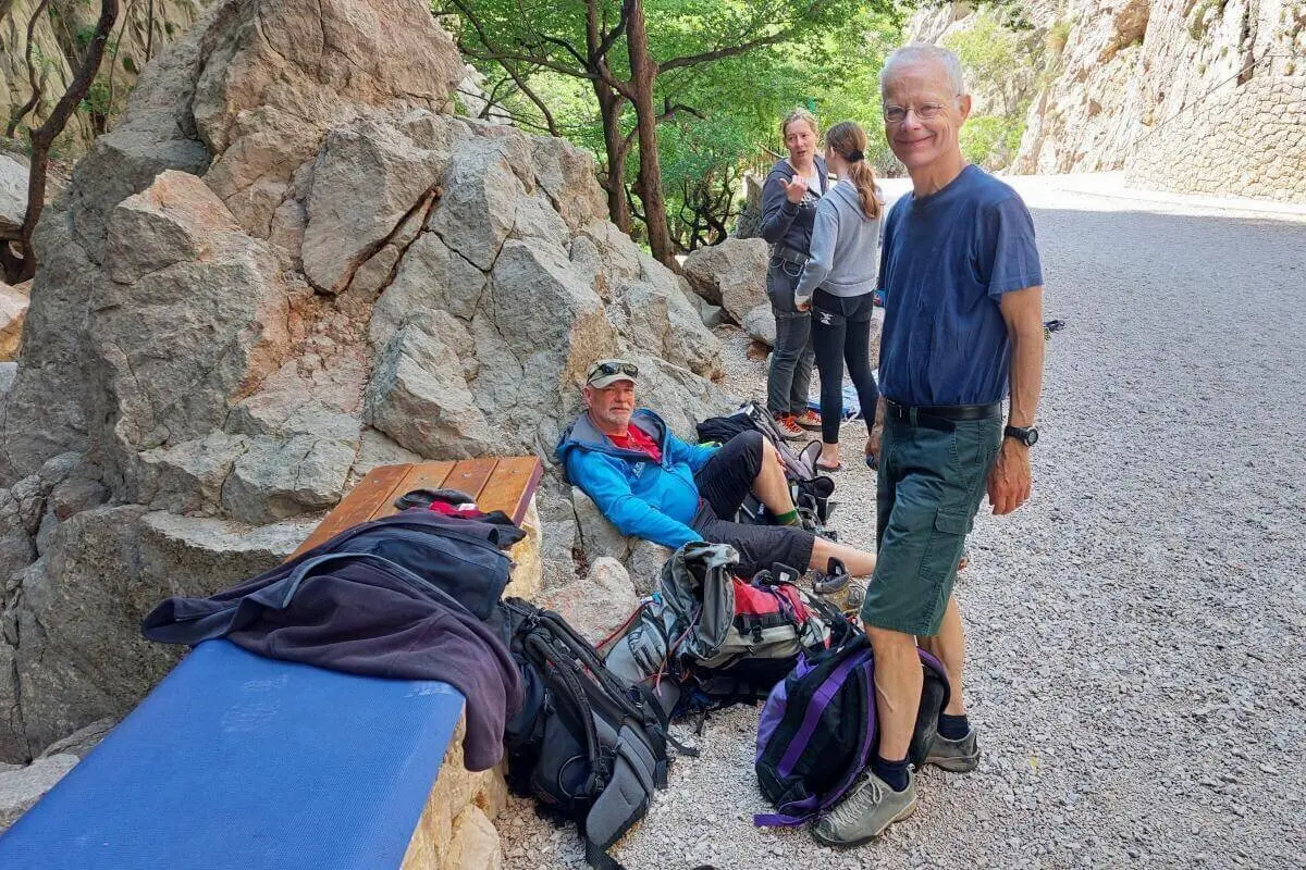 Fünf Personen ruhen an einem schattigen Platz mit Felsen und Bäumen; Rucksäcke und Ausrüstung liegen bereit. | © DAV Markt Schwaben | Foto Lutz Gründel