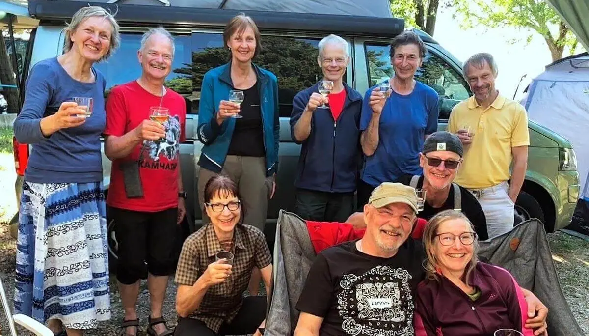 Zehn Erwachsene feiern vor Campervan; zwei sitzen vorn, andere stehen lachend im Hintergrund. | © DAV Markt Schwaben | Foto Hildegard Petschik