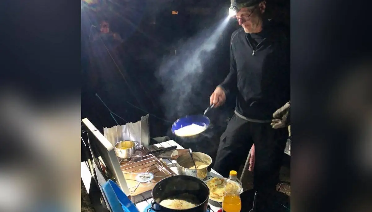 Eine Person kocht bei Dunkelheit mit Stirnlampe am Gaskocher; Dampf steigt aus Pfanne und Töpfen. | © DAV Markt Schwaben | Foto Hildegard Petschik