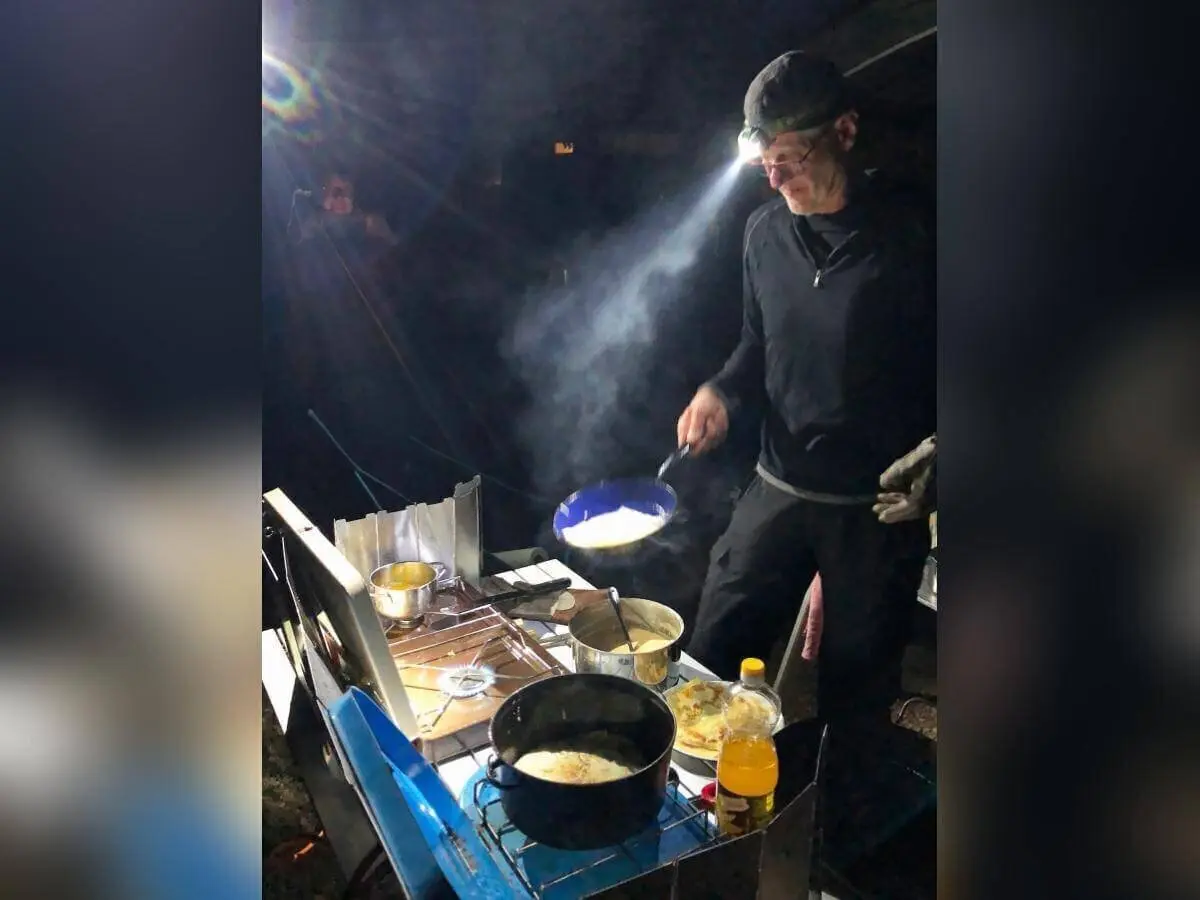 Eine Person kocht bei Dunkelheit mit Stirnlampe am Gaskocher; Dampf steigt aus Pfanne und Töpfen. | © DAV Markt Schwaben | Foto Hildegard Petschik