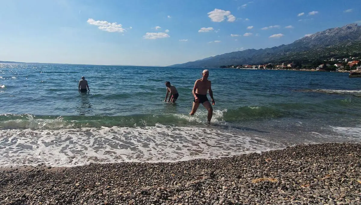 Vier Personen genießen das Meer bei Sonnenschein; Kiesstrand und Küstenstadt im Hintergrund. | © DAV Markt Schwaben | Foto Karin und Peter Tkaczuk