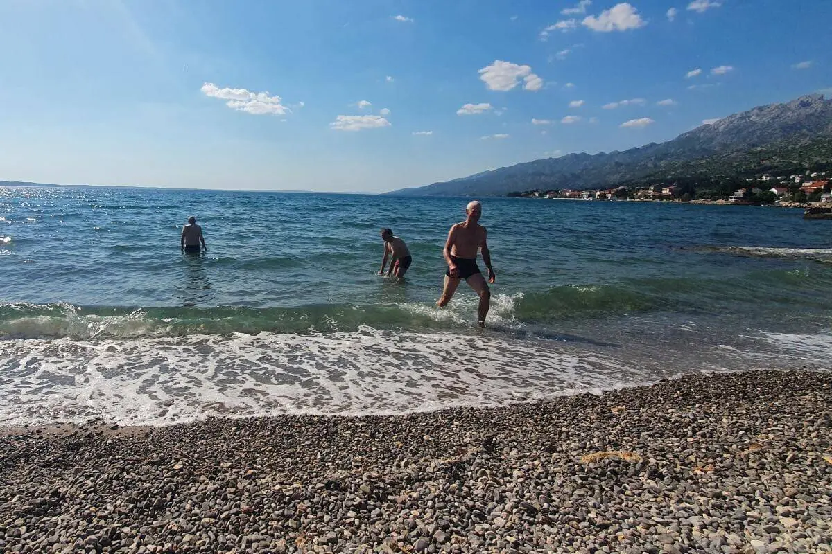 Vier Personen genießen das Meer bei Sonnenschein; Kiesstrand und Küstenstadt im Hintergrund. | © DAV Markt Schwaben | Foto Karin und Peter Tkaczuk