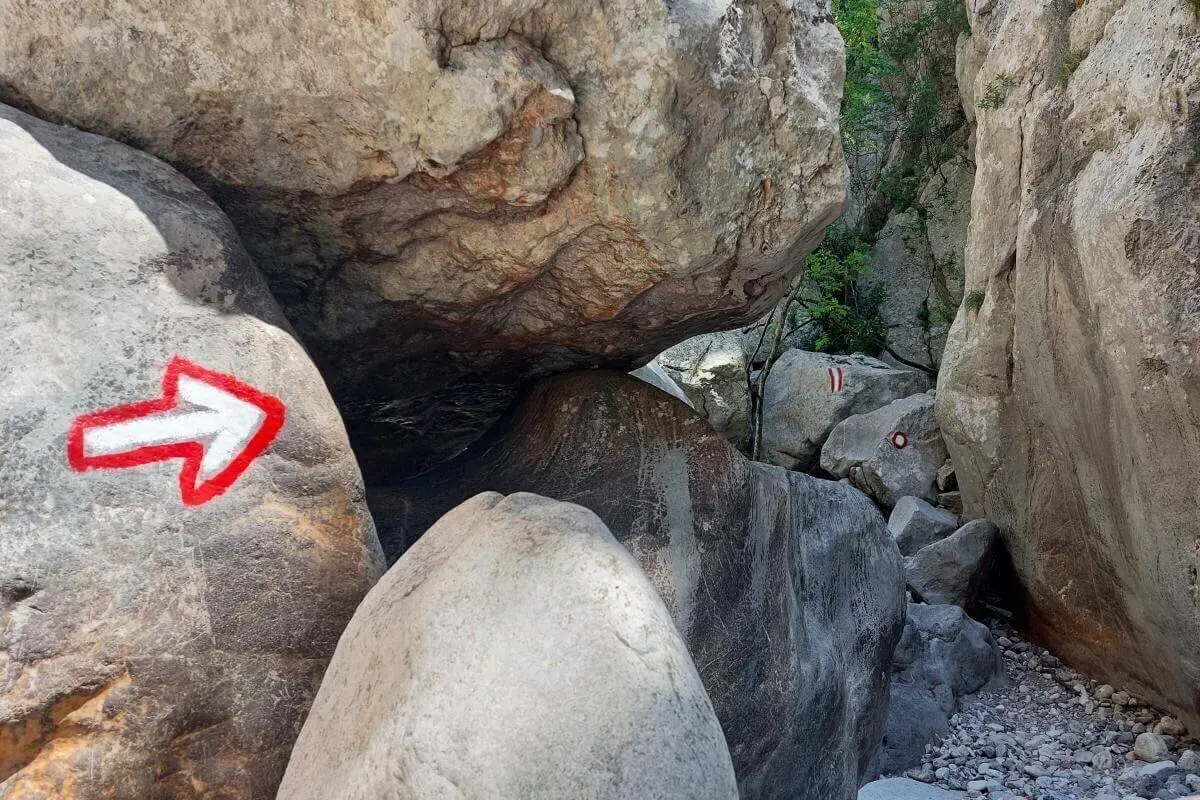 Rote Markierungen auf Felsen weisen durch schmale Passage; grobes Gelände mit wenig Vegetation. | © DAV Markt Schwaben | Foto Lutz Gründel