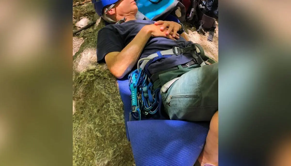 Eine Person mit Helm und Klettergurt ruht auf Schaumstoffmatte zwischen Felsen; Ausrüstung liegt daneben. | © DAV Markt Schwaben | Foto Hildegard Petschik