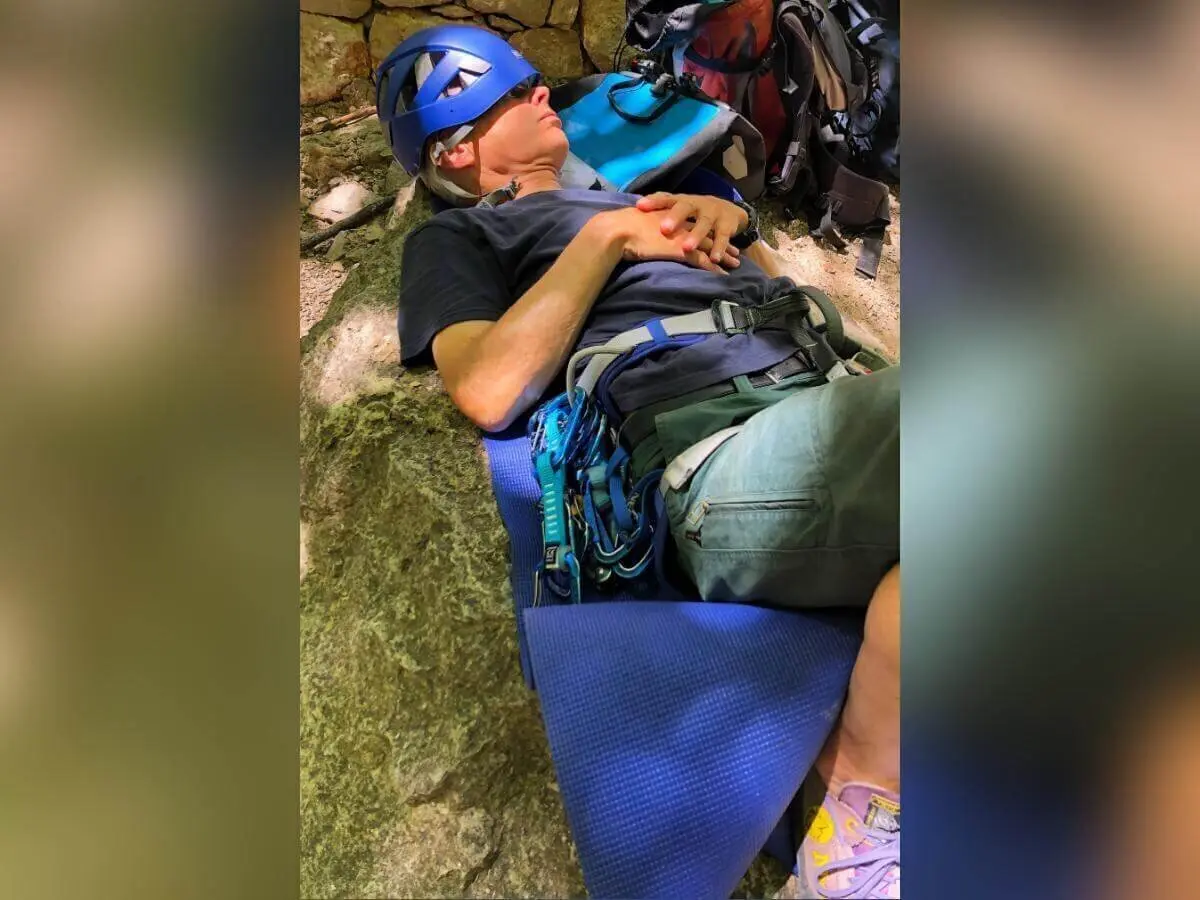 Eine Person mit Helm und Klettergurt ruht auf Schaumstoffmatte zwischen Felsen; Ausrüstung liegt daneben. | © DAV Markt Schwaben | Foto Hildegard Petschik