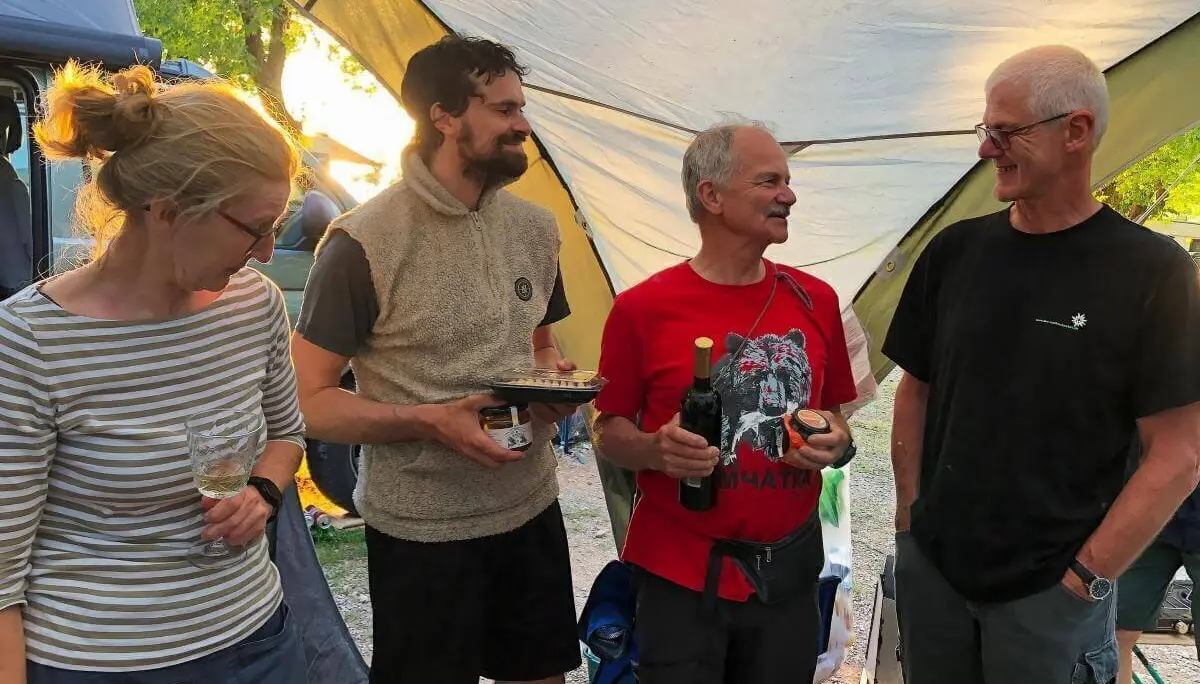 Vier Personen unter Pavillon mit Wein und Speisen; lockere Stimmung bei Campingausrüstung und Bäumen. | © DAV Markt Schwaben | Foto Hildegard Petschik