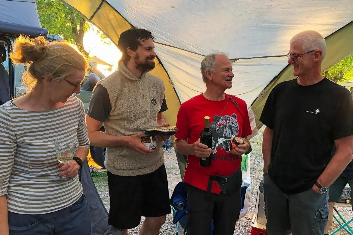 Vier Personen unter Pavillon mit Wein und Speisen; lockere Stimmung bei Campingausrüstung und Bäumen. | © DAV Markt Schwaben | Foto Hildegard Petschik