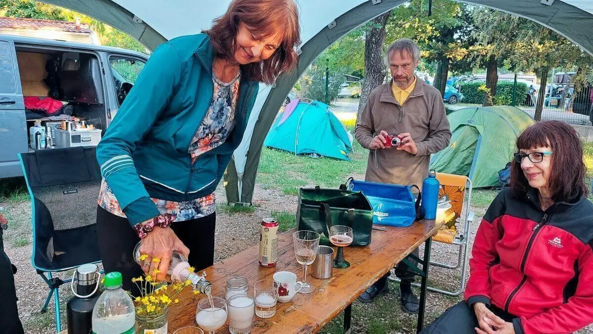 Vier Personen unter Pavillon beim Einschenken von Getränken; Blumenstrauß und Zelte im Hintergrund. | © DAV Markt Schwaben | Foto Lutz Gründel