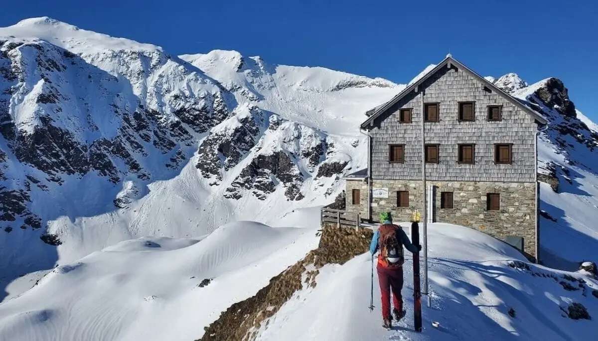 Ein Bergsteiger sitzt mit Ausrüstung neben dem Niedersachsenhaus auf schneebedecktem Hang – im Sonnenlicht eröffnet sich der Blick auf die Schareck-Nordwand. | © DAV Markt Schwaben | Foto: Walter Kressirer