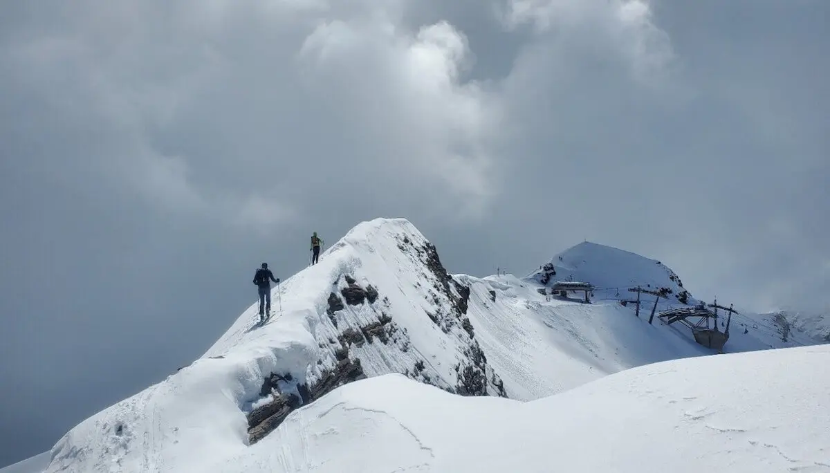 Zwei Bergsteiger folgen dem verschneiten Südgrat vom Gipfel des Schareck – im Hintergrund die Baumbachspitze und die Bergstation des Skigebiets, dahinter weite Firnhänge unter leicht bewölktem Himmel. | © DAV Markt Schwaben | Foto: Walter Kressirer