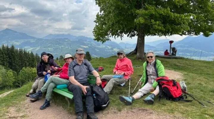 Seniorengruppe macht Pause auf Holzbank mit Bergblick in Oberaudorf. Wolkiger Himmel, entspannte Stimmung. | © DAV Markt Schwaben | Foto Hubert Inhofer