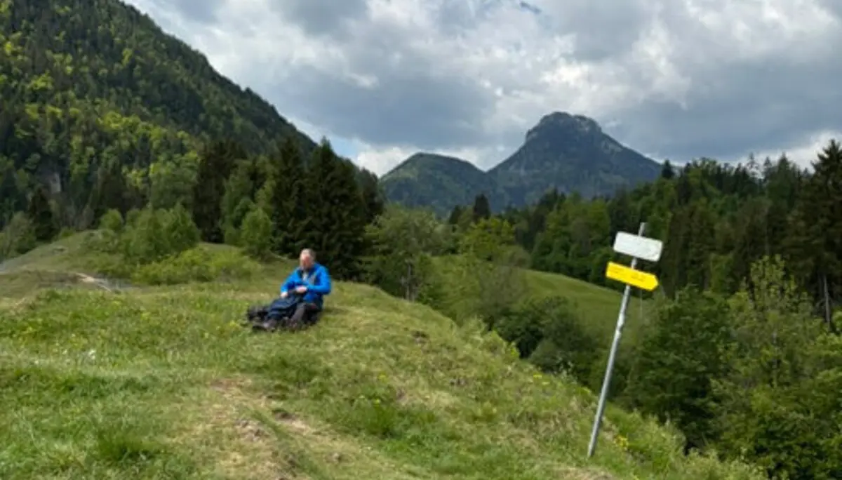Seniorengruppe auf Wanderung bei Oberaudorf – Pause auf einer Holzbank mit Bergblick unter wolkigem Himmel. | © DAV Markt Schwaben | Foto Hubert Inhofer