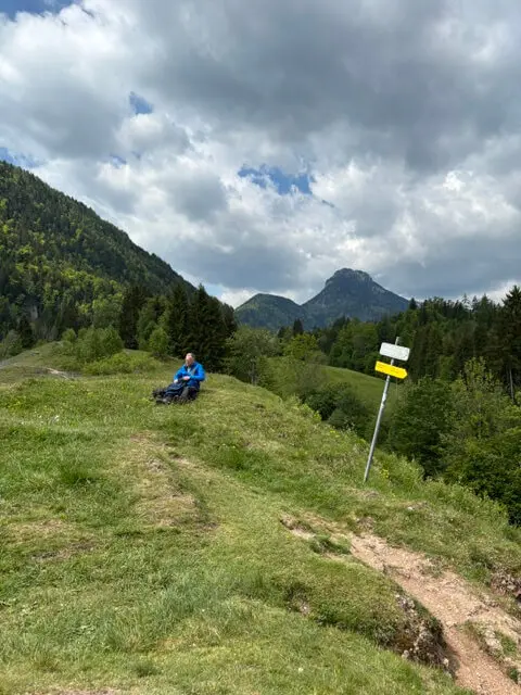 Seniorengruppe auf Wanderung bei Oberaudorf – Pause auf einer Holzbank mit Bergblick unter wolkigem Himmel. | © DAV Markt Schwaben | Foto Hubert Inhofer