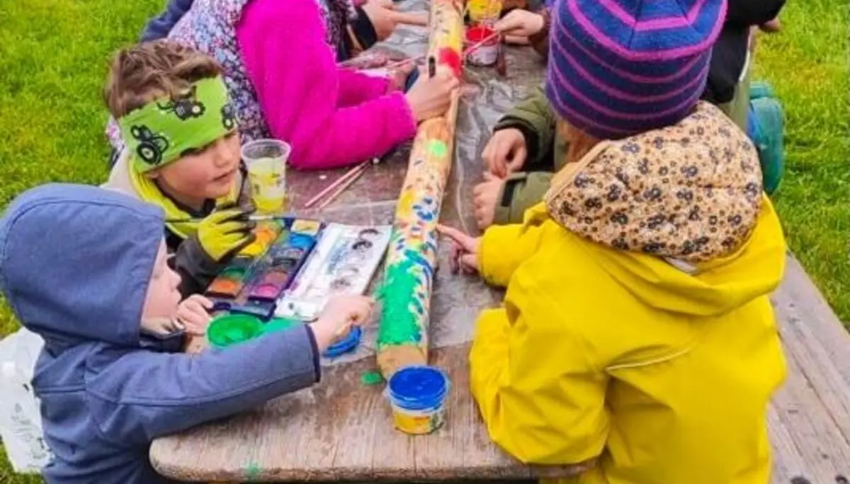 Eine Gruppe von Kindern steht im Freien um einen Tisch und dekoriert ein Buch. Sie sind vertieft in ihre kreative Arbeit. | © DAV Markt Schwaben | Foto: Familiengruppe