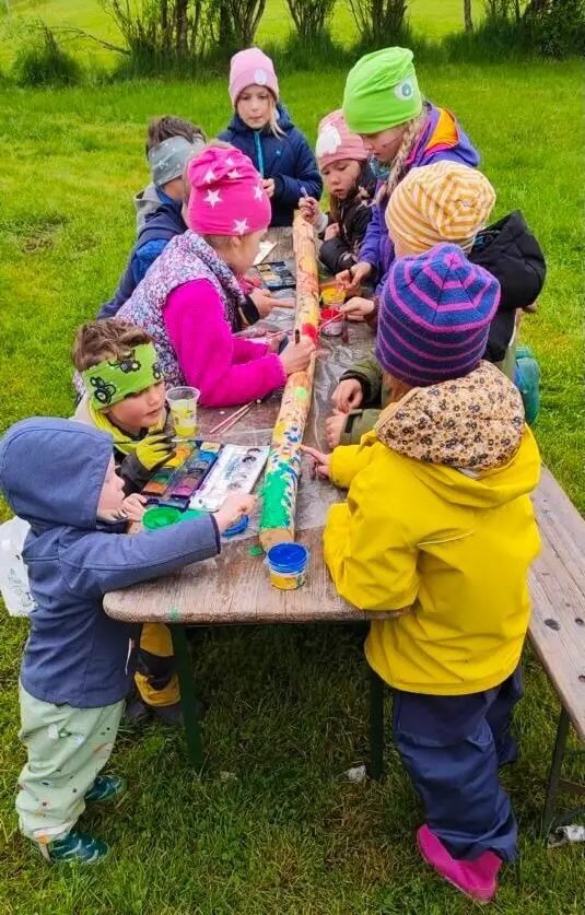 Eine Gruppe von Kindern steht im Freien um einen Tisch und dekoriert ein Buch. Sie sind vertieft in ihre kreative Arbeit. | © DAV Markt Schwaben | Foto: Familiengruppe