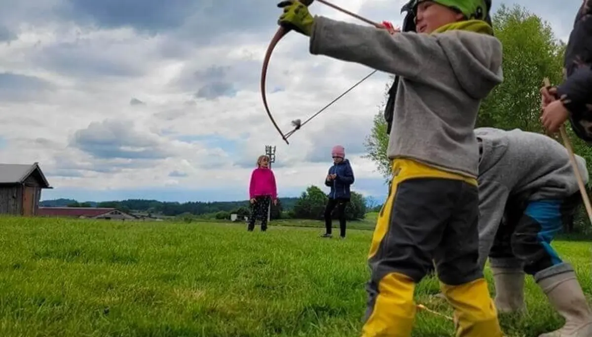 Ein Kind steht im Freien und hält Pfeil und Bogen. Es wirkt konzentriert, während es sich auf sein Ziel vorbereitet. | © DAV Markt Schwaben | Foto: Familiengruppe