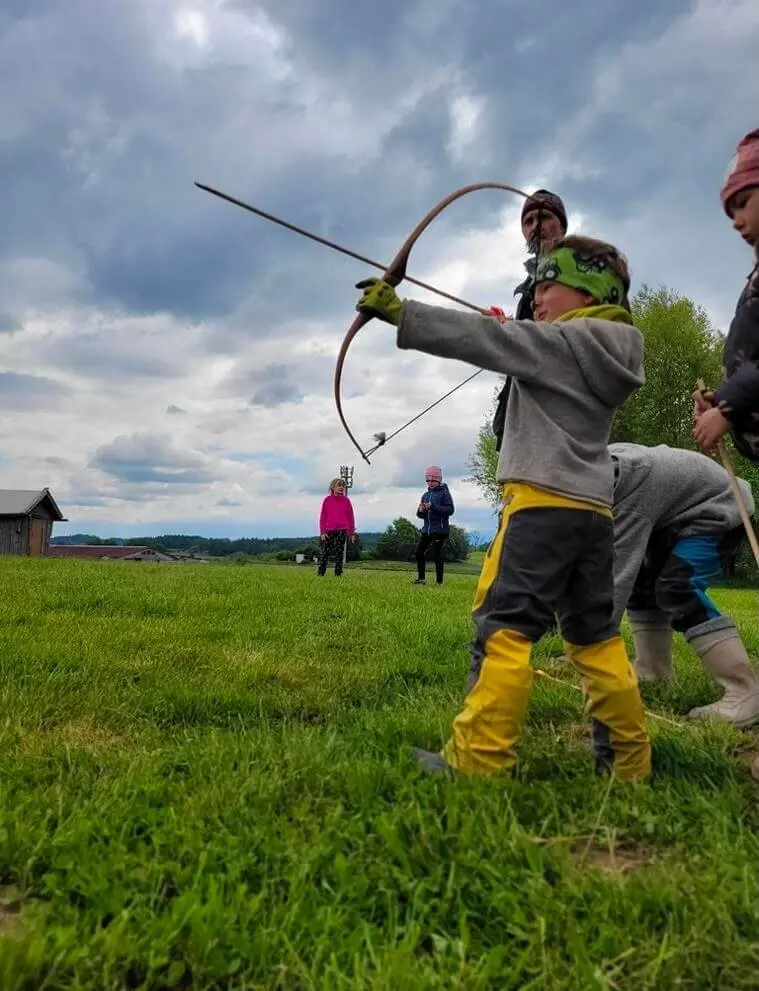 Ein Kind steht im Freien und hält Pfeil und Bogen. Es wirkt konzentriert, während es sich auf sein Ziel vorbereitet. | © DAV Markt Schwaben | Foto: Familiengruppe