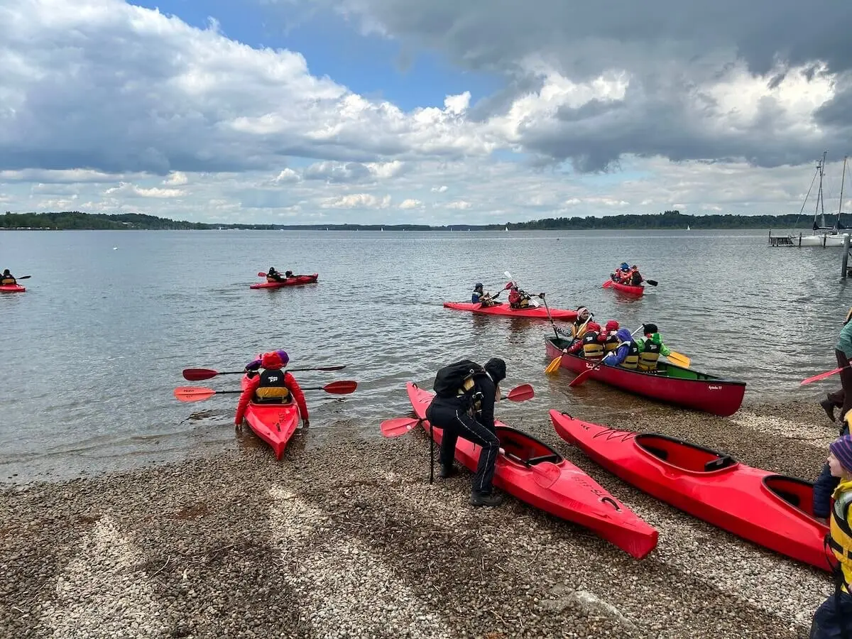 Mehrere Kanus liegen am Ufer eines Sees, während Kinder und Erwachsene sich darauf vorbereiten, einzusteigen. | © DAV Markt Schwaben | Foto: Familiengruppe