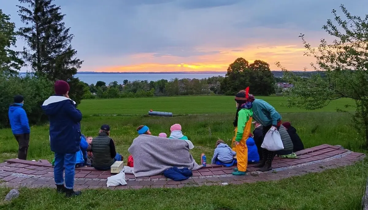Eine Gruppe von Menschen sitzt auf halbrunden Steinstufen im Freien und posiert für ein Foto. Die Umgebung ist grün und von Bäumen umgeben. | © DAV Markt Schwaben | Foto: Familiengruppe