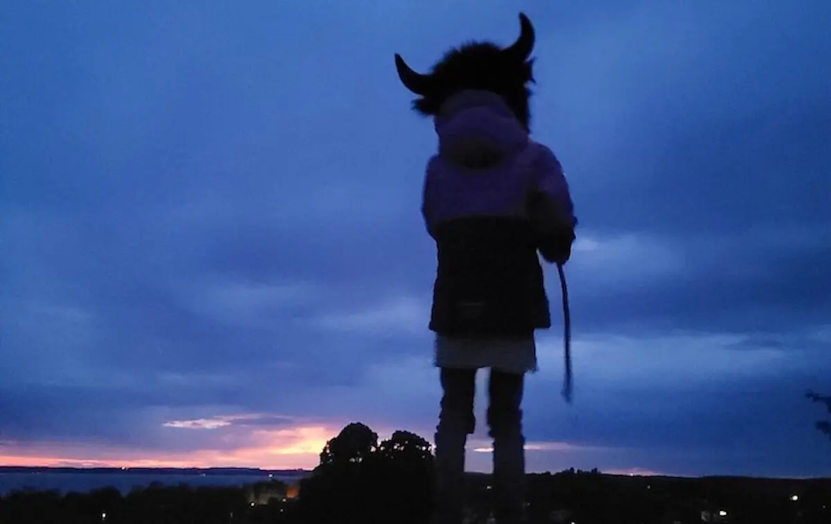 Eine Person mit einem Hut mit Hörnern steht bei Sonnenuntergang auf einem Hügel. Der Himmel leuchtet in warmen Blau- und Orangetönen. | © DAV Markt Schwaben | Foto: Familiengruppe