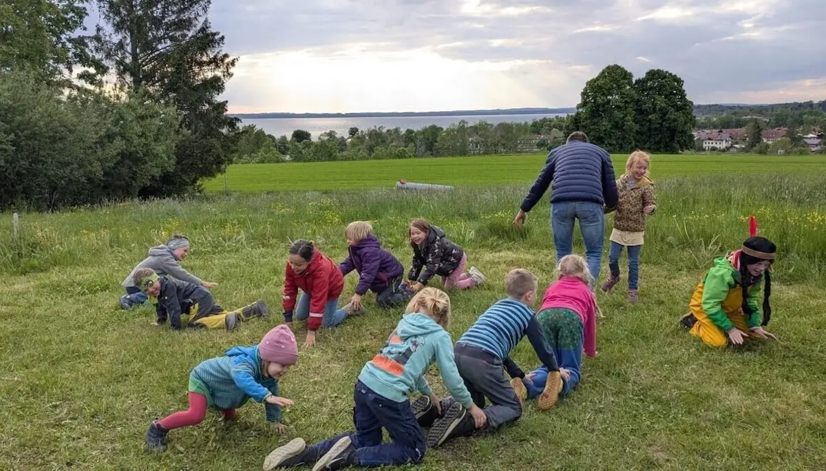 Eine Gruppe von Kindern spielt fröhlich mit einem Erwachsenen auf einer grünen Wiese. Sie bewegen sich aktiv und genießen die gemeinsame Zeit. | © DAV Markt Schwaben | Foto: Familiengruppe