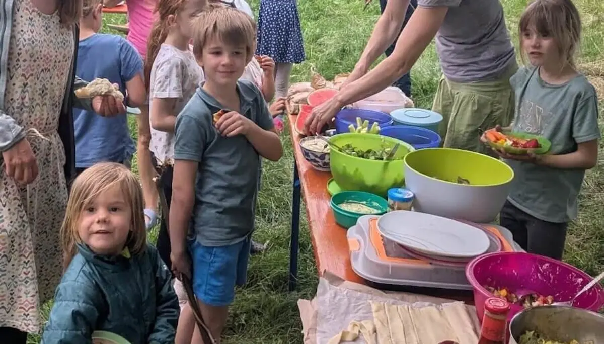 Kinder und Erwachsene versammeln sich an einem gedeckten Tisch mit Salaten und Grillgut – geselliges Familienpicknick im Freien. | © DAV Markt Schwaben | Foto Silke Titze