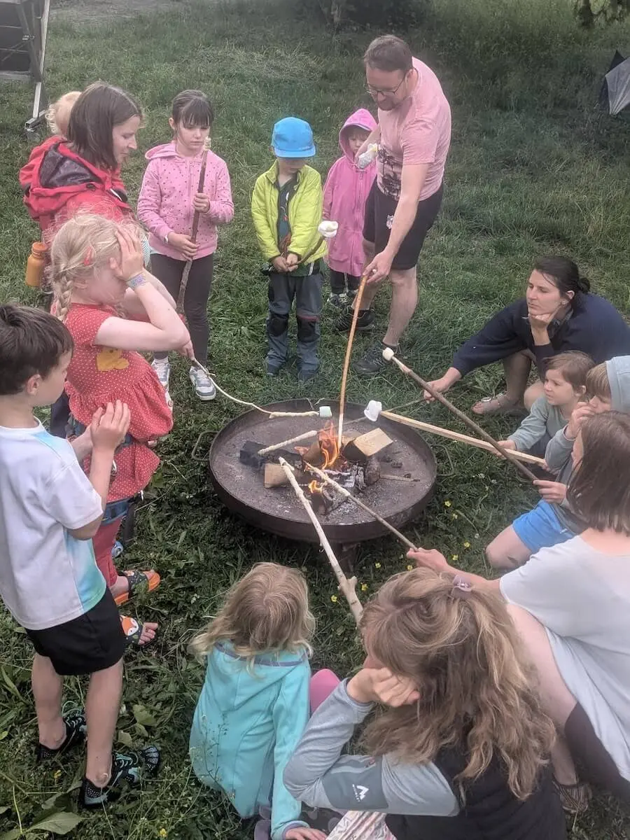 Kinder und Erwachsene sitzen rund ums Lagerfeuer und rösten Marshmallows – fröhliches Beisammensein. | © DAV Markt Schwaben | Foto Silke Titze