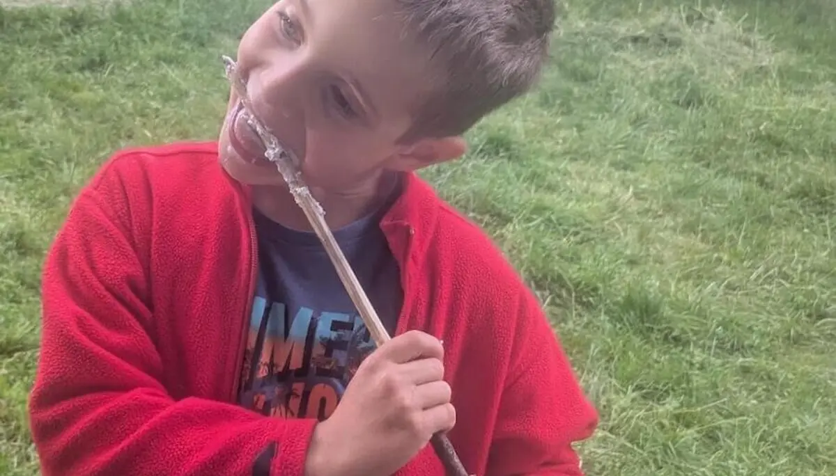 Ein Kind steht auf einer Wiese und isst genüsslich Stockbrot direkt vom Stock – ein Moment voller Natur und Lagerfeuerfreude. | © DAV Markt Schwaben | Foto Silke Titze