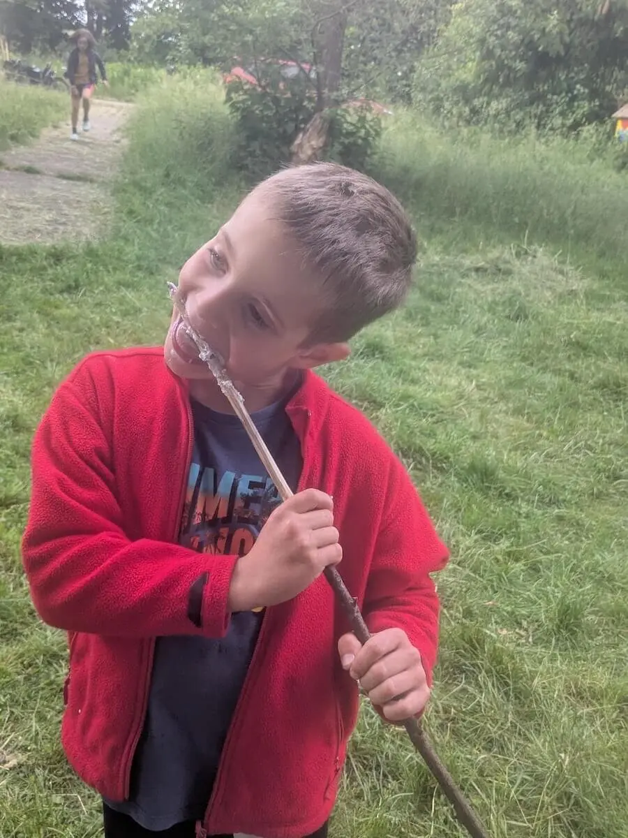 Ein Kind steht auf einer Wiese und isst genüsslich Stockbrot direkt vom Stock – ein Moment voller Natur und Lagerfeuerfreude. | © DAV Markt Schwaben | Foto Silke Titze