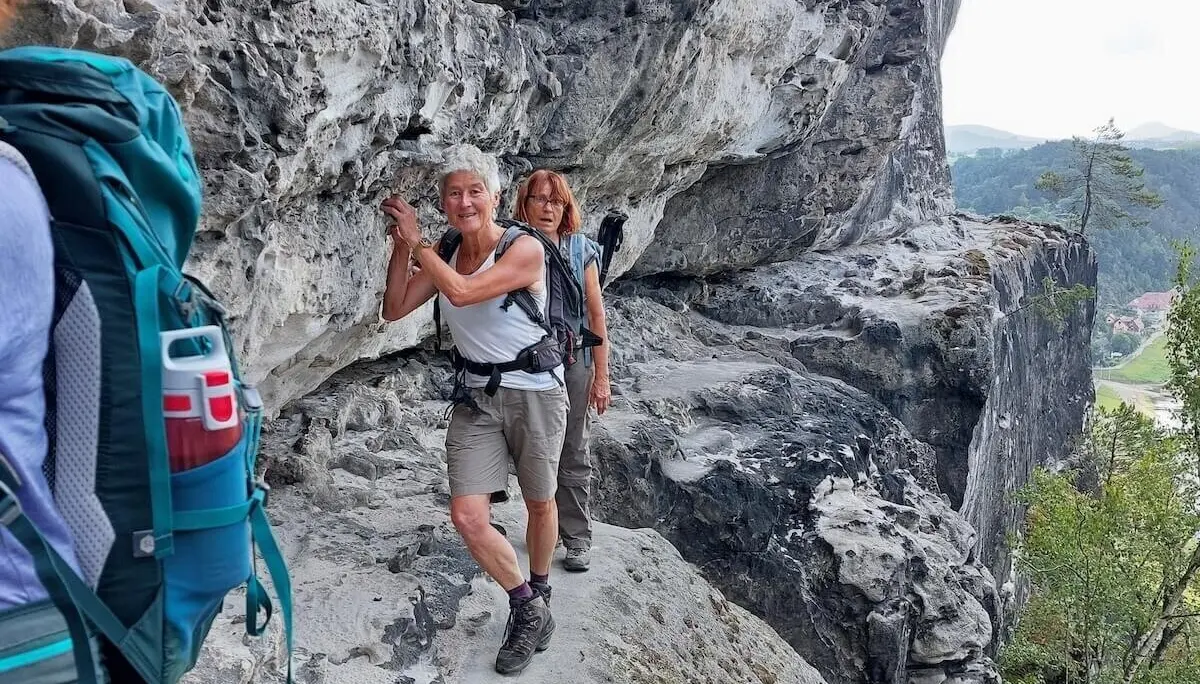 Drei Personen steigen auf schmalem Felsband entlang, rechts steiler Abgrund, im Hintergrund bewaldetes Tal. | © DAV Markt Schwaben | Foto Lutz Gründel