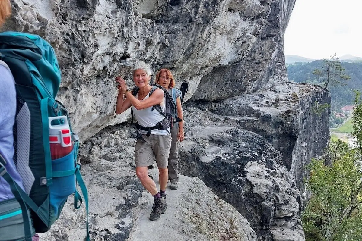 Drei Personen steigen auf schmalem Felsband entlang, rechts steiler Abgrund, im Hintergrund bewaldetes Tal. | © DAV Markt Schwaben | Foto Lutz Gründel
