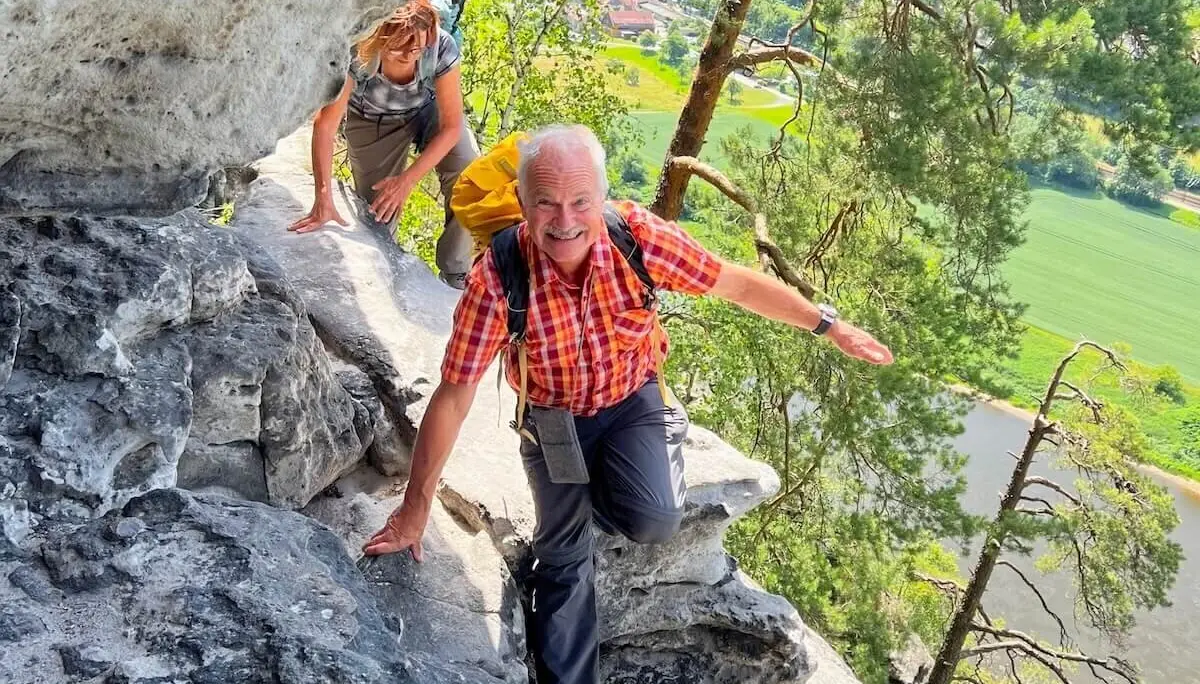 Zwei Wandernde erklimmen steile Felswand, unten Fluss und Häuser, vorne Person mit gelbem Rucksack im Gleichgewicht. | © DAV Markt Schwaben | Foto Edith Zerrle