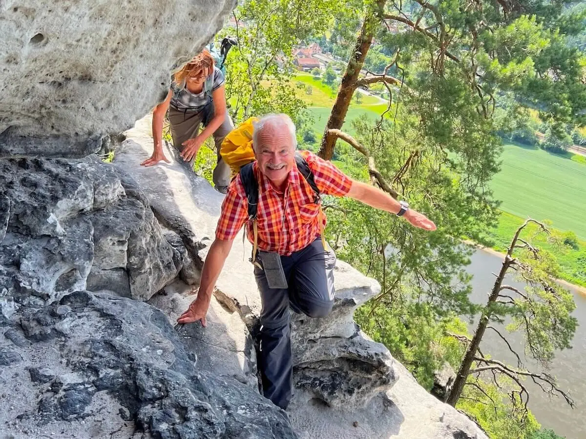 Zwei Wandernde erklimmen steile Felswand, unten Fluss und Häuser, vorne Person mit gelbem Rucksack im Gleichgewicht. | © DAV Markt Schwaben | Foto Edith Zerrle