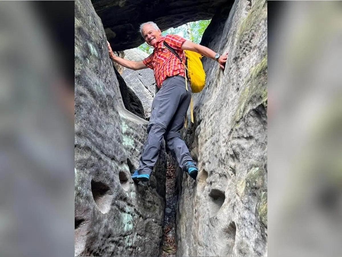 Wandernde Person mit gelbem Rucksack nutzt Trittkerben in schmaler Felsspalte, umgeben von rauer Steinstruktur. | © DAV Markt Schwaben | Foto Edith Zerrle