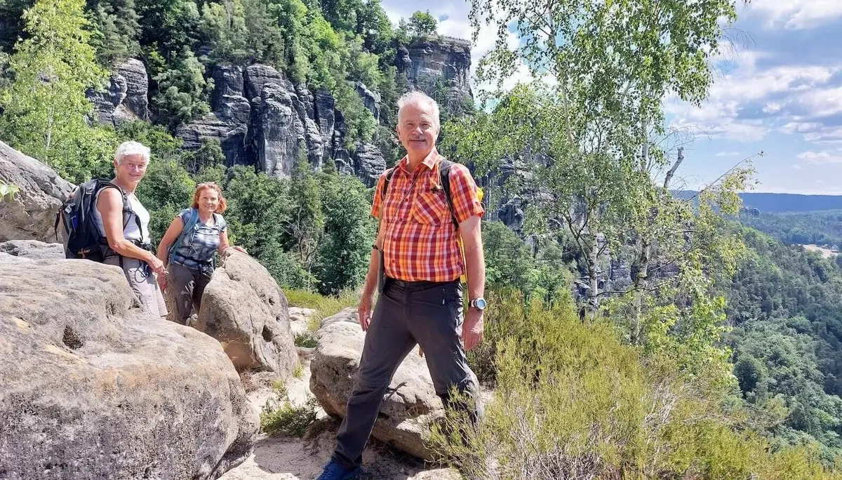 Drei Personen stehen auf felsigem Pfad vor steilen Klippen, umgeben von Wald und großen Felsbrocken. | © DAV Markt Schwaben | Foto Michaela Haaß