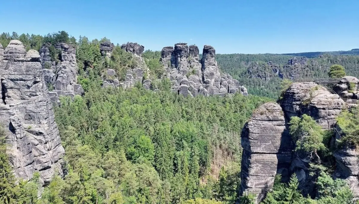 Hohe Felsnadeln ragen aus Wald, rechts verbindet schmale Brücke zwei Felsen, Himmel klar und sonnig. | © DAV Markt Schwaben | Foto Michaela Haaß