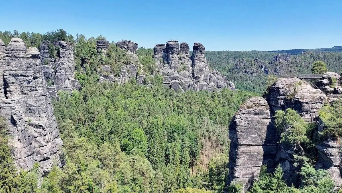 Hohe Felsnadeln ragen aus Wald, rechts verbindet schmale Brücke zwei Felsen, Himmel klar und sonnig. | © DAV Markt Schwaben | Foto Michaela Haaß