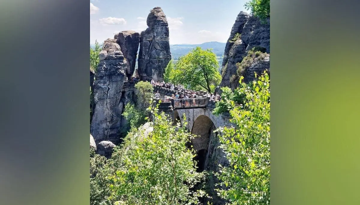 Zahlreiche Menschen überqueren steinerne Basteibrücke zwischen Felsen, umgeben von Wald und blauem Himmel. | © DAV Markt Schwaben | Foto Michaela Haaß