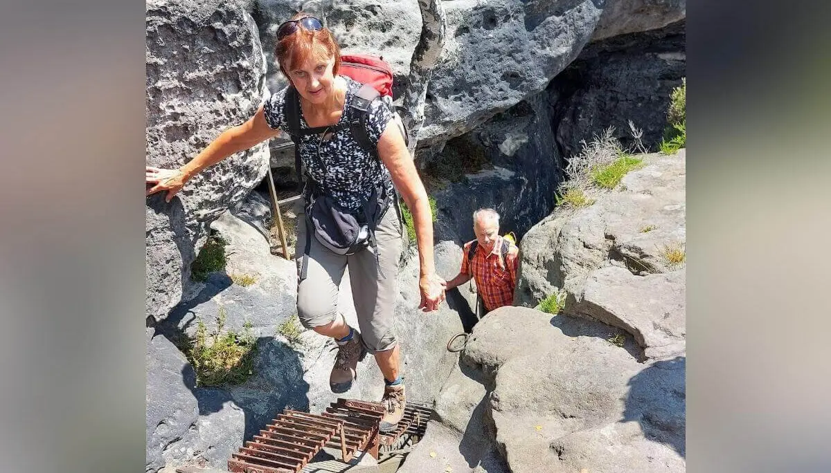 Zwei Personen steigen Metallleiter und Felsstufen hinauf, nutzen Handlauf, umgeben von steilem Gelände. | © DAV Markt Schwaben | Foto Michaela Haaß