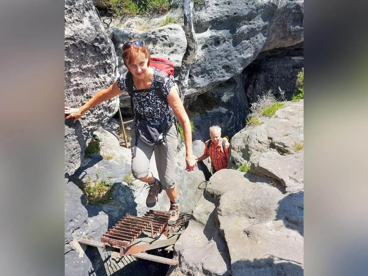 Zwei Personen steigen Metallleiter und Felsstufen hinauf, nutzen Handlauf, umgeben von steilem Gelände. | © DAV Markt Schwaben | Foto Michaela Haaß