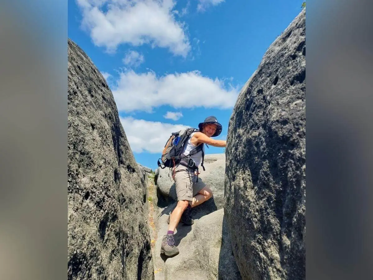 Person mit Sonnenhut und Rucksack klettert zwischen zwei Felsen, blauer Himmel im Hintergrund. | © DAV Markt Schwaben | Foto Angelika Göthe-Volkert