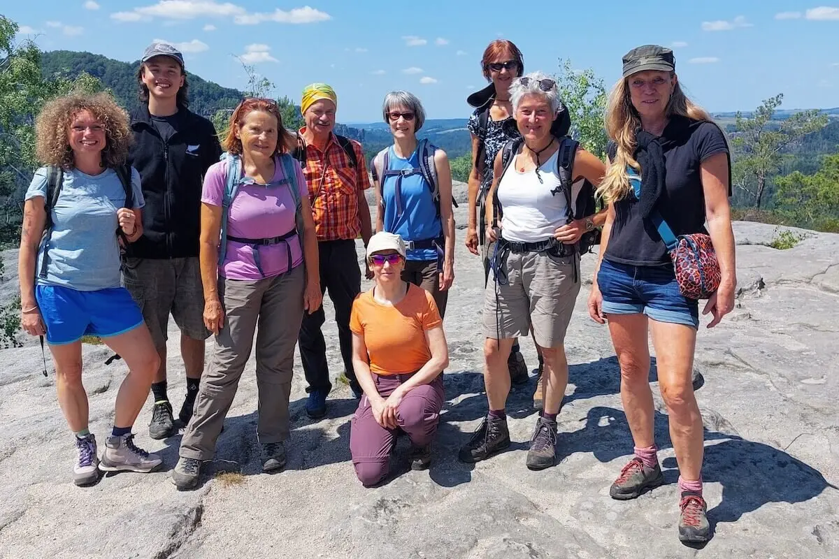 Neun Personen posieren auf Felsplateau mit Blick auf Hügel und Wald, Himmel leicht bewölkt. | © DAV Markt Schwaben | Foto Lutz Gründel