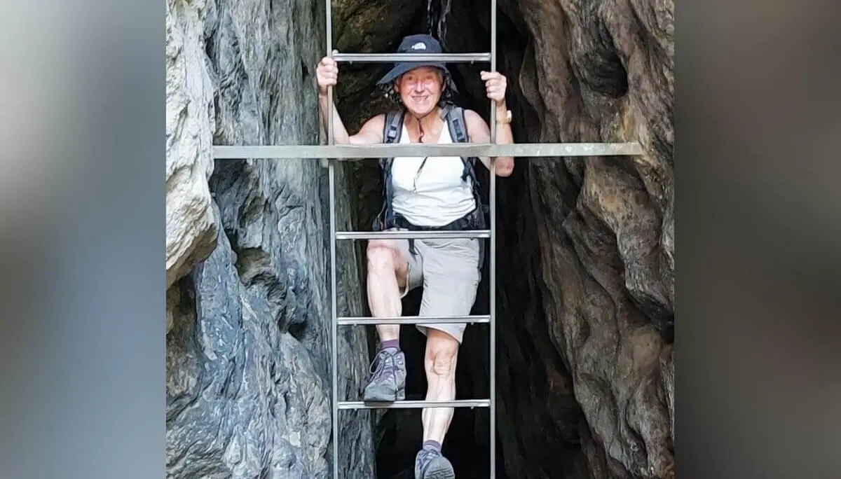 Person mit Sonnenhut steigt Metallleiter in schmaler Felsspalte hinauf, umgeben von rauem Gestein. | © DAV Markt Schwaben | Foto Lutz Gründel