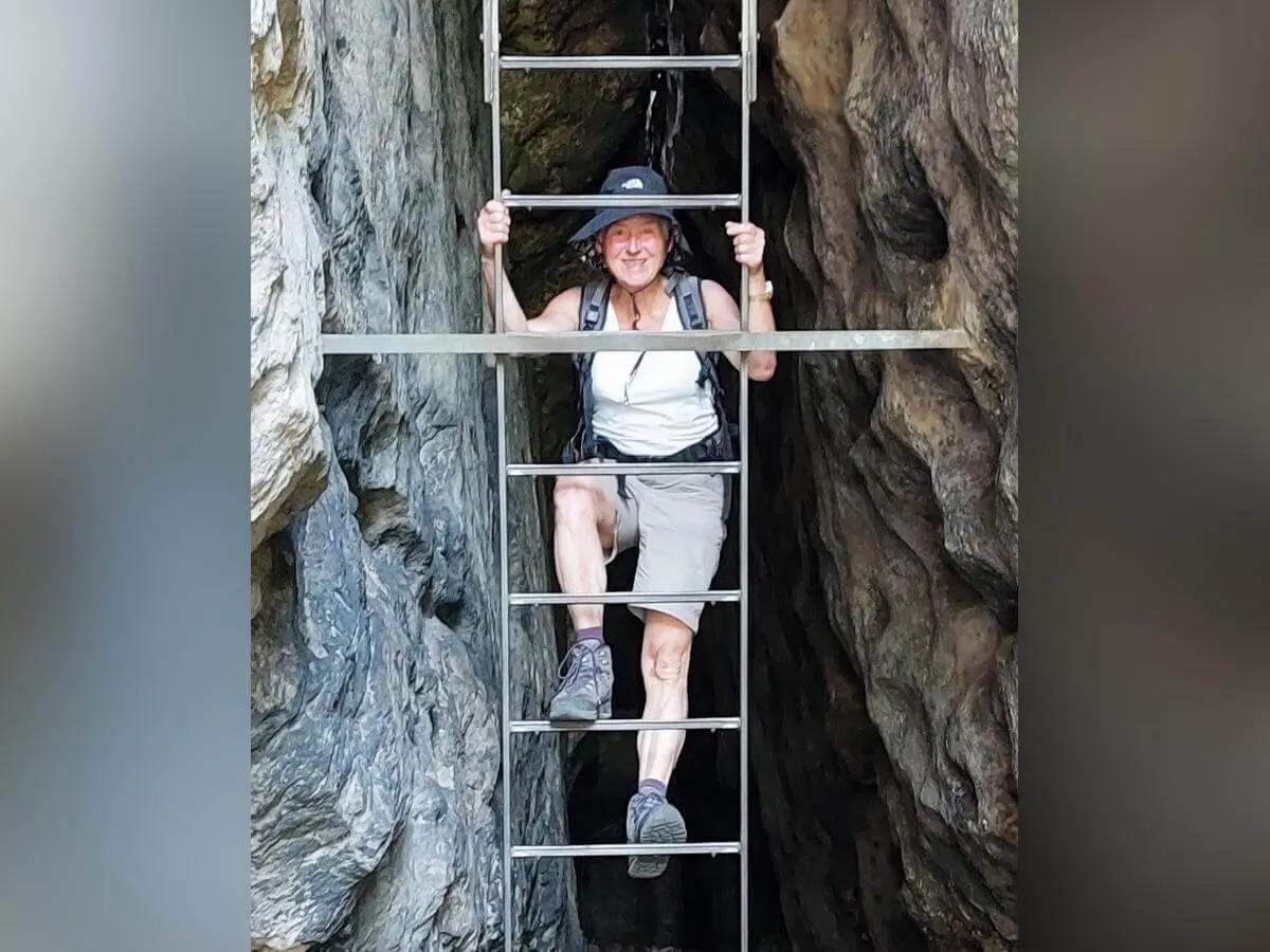 Person mit Sonnenhut steigt Metallleiter in schmaler Felsspalte hinauf, umgeben von rauem Gestein. | © DAV Markt Schwaben | Foto Lutz Gründel