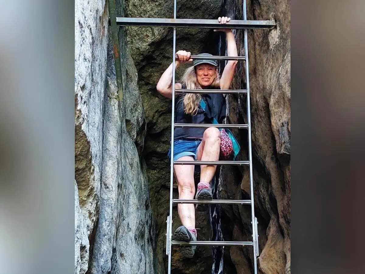 Person mit bunter Tasche steigt senkrechte Leiter zwischen Felswänden, umgeben von rauer Struktur. | © DAV Markt Schwaben | Foto Lutz Gründel