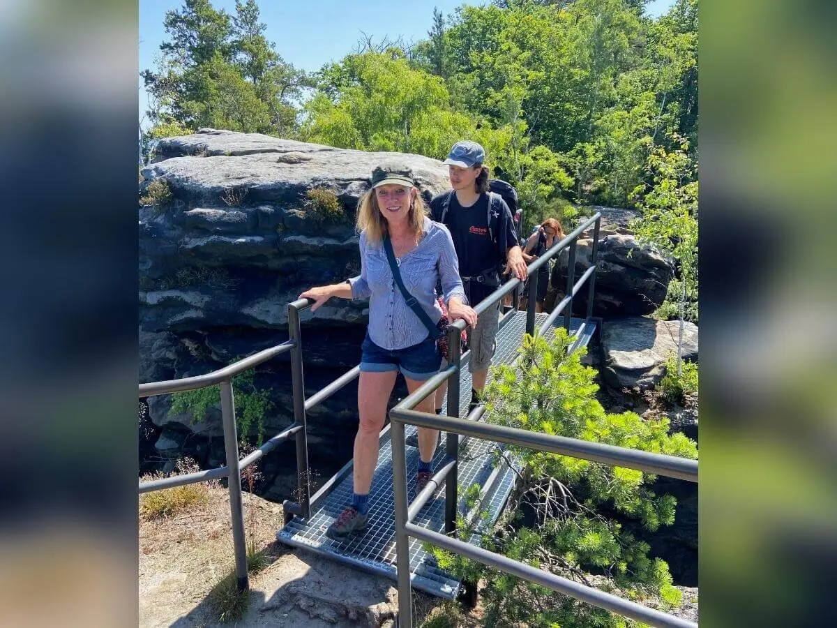 Zwei Personen überqueren Metallbrücke, links Felswand, rechts dichter Wald, sonniger Tag. | © DAV Markt Schwaben | Foto Yvonne Haaß
