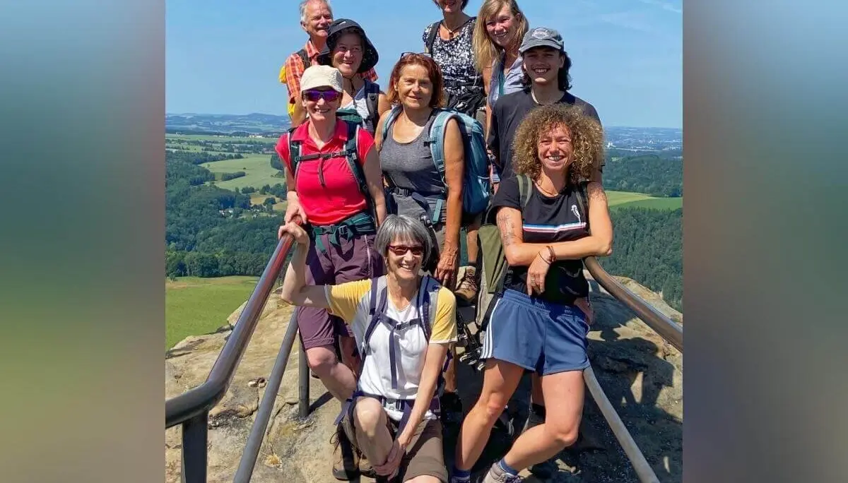 Neun Personen posieren auf Plattform mit Geländer, dahinter weite Landschaft mit Feldern und Hügeln. | © DAV Markt Schwaben | Foto Yvonne Haaß