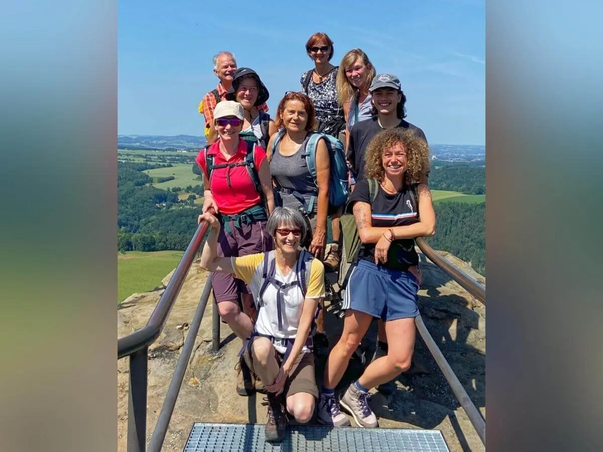 Neun Personen posieren auf Plattform mit Geländer, dahinter weite Landschaft mit Feldern und Hügeln. | © DAV Markt Schwaben | Foto Yvonne Haaß